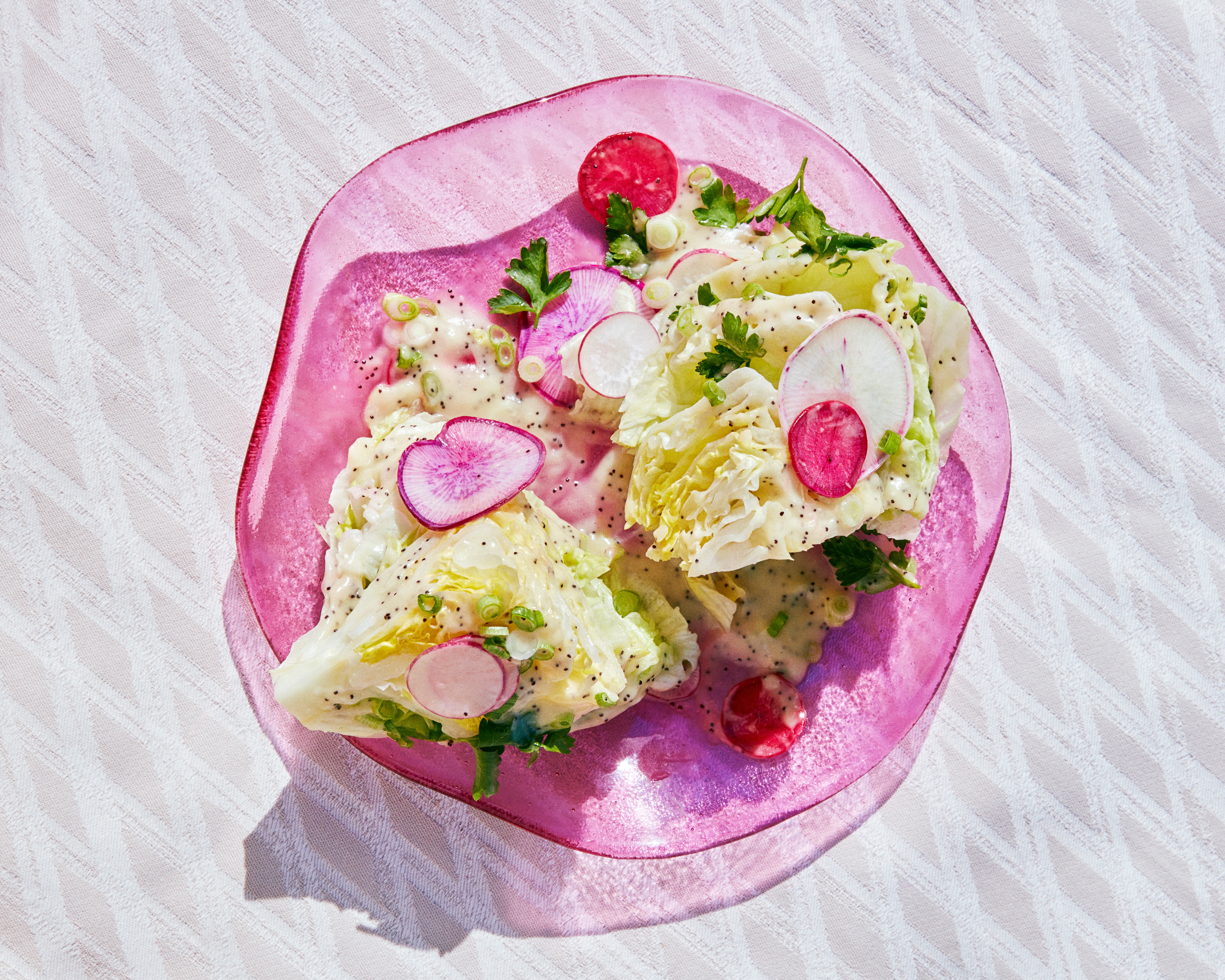 A wedge salad with iceberg lettuce, miso-poppy dressing, and radishes, served on a pink plate.