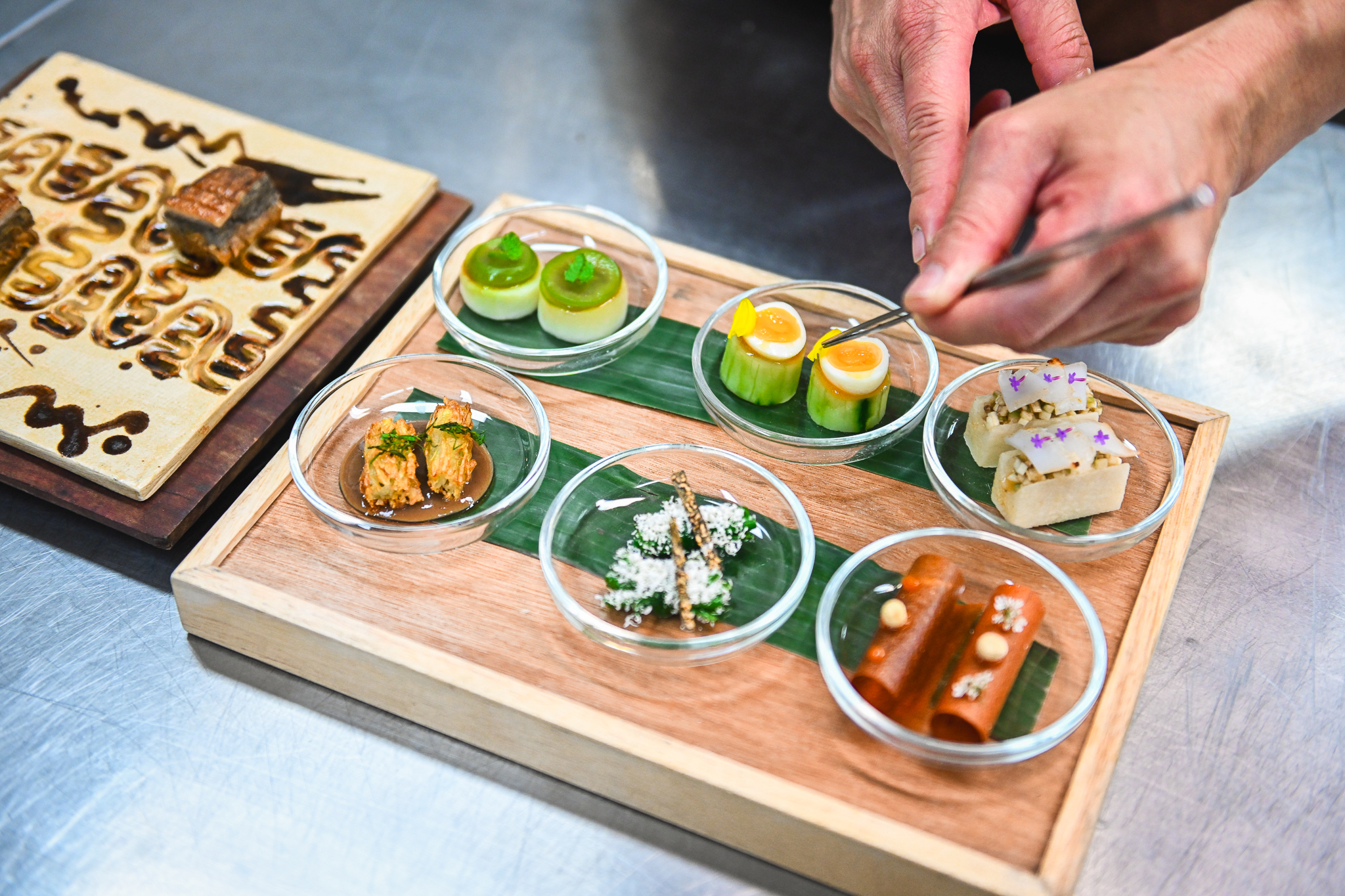 A chef plates a large board containing six colorful dishes.