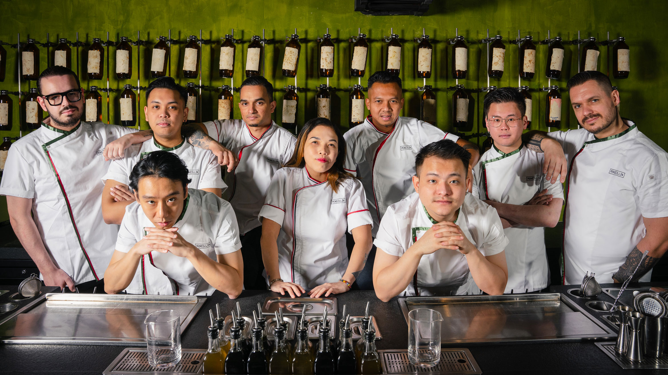A group of people wearing white jackets poses behind a bar.
