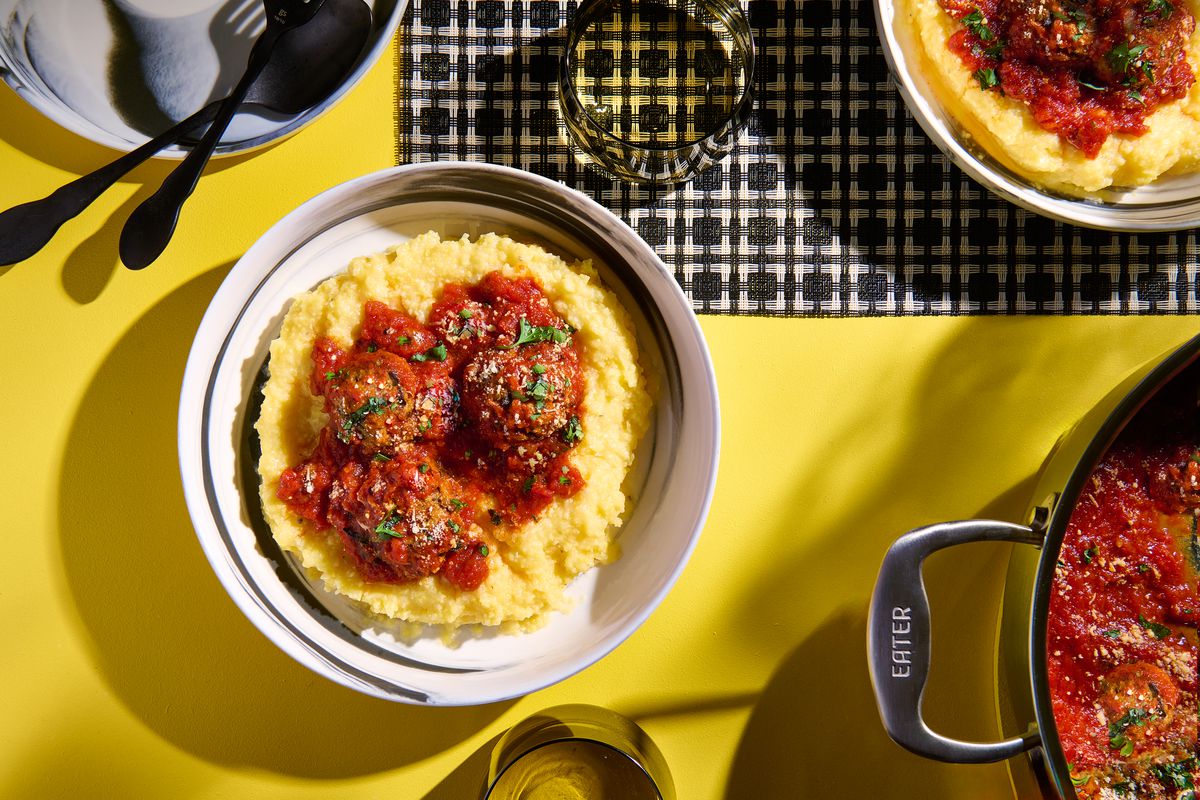 A bowl of eggplant meatballs atop polenta, served on a bright yellow table. 