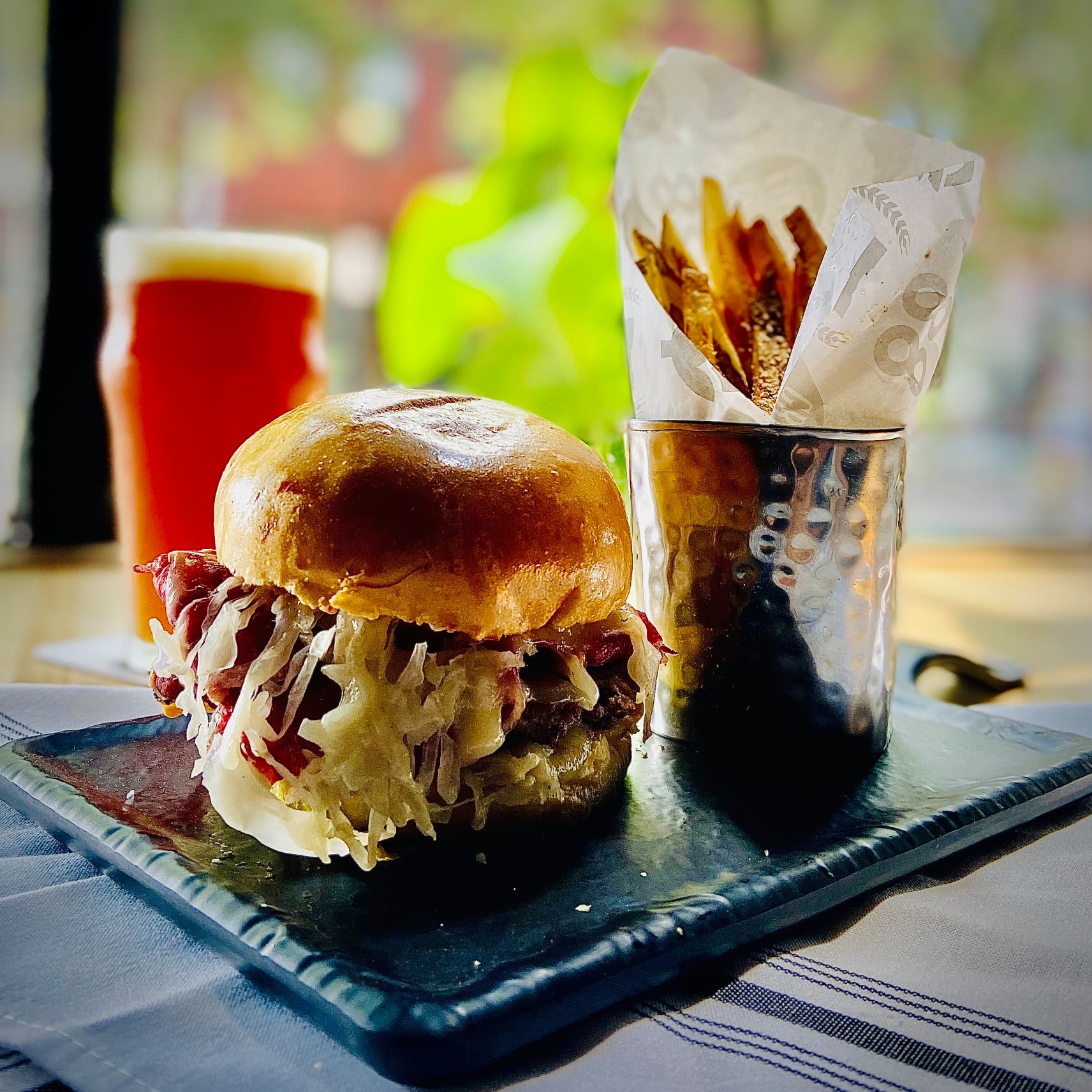 A burger topped with sauerkraut, swiss, and sauce with a beer in the background.